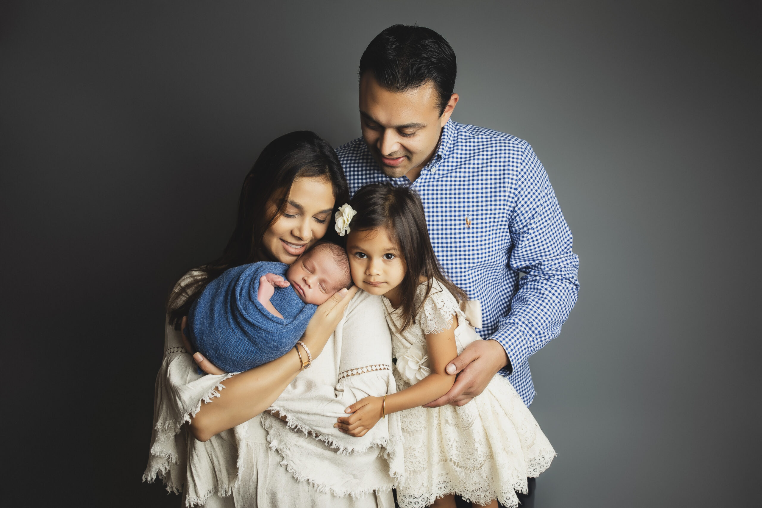 Smiling family looking at newborn against gray background in Austin TX