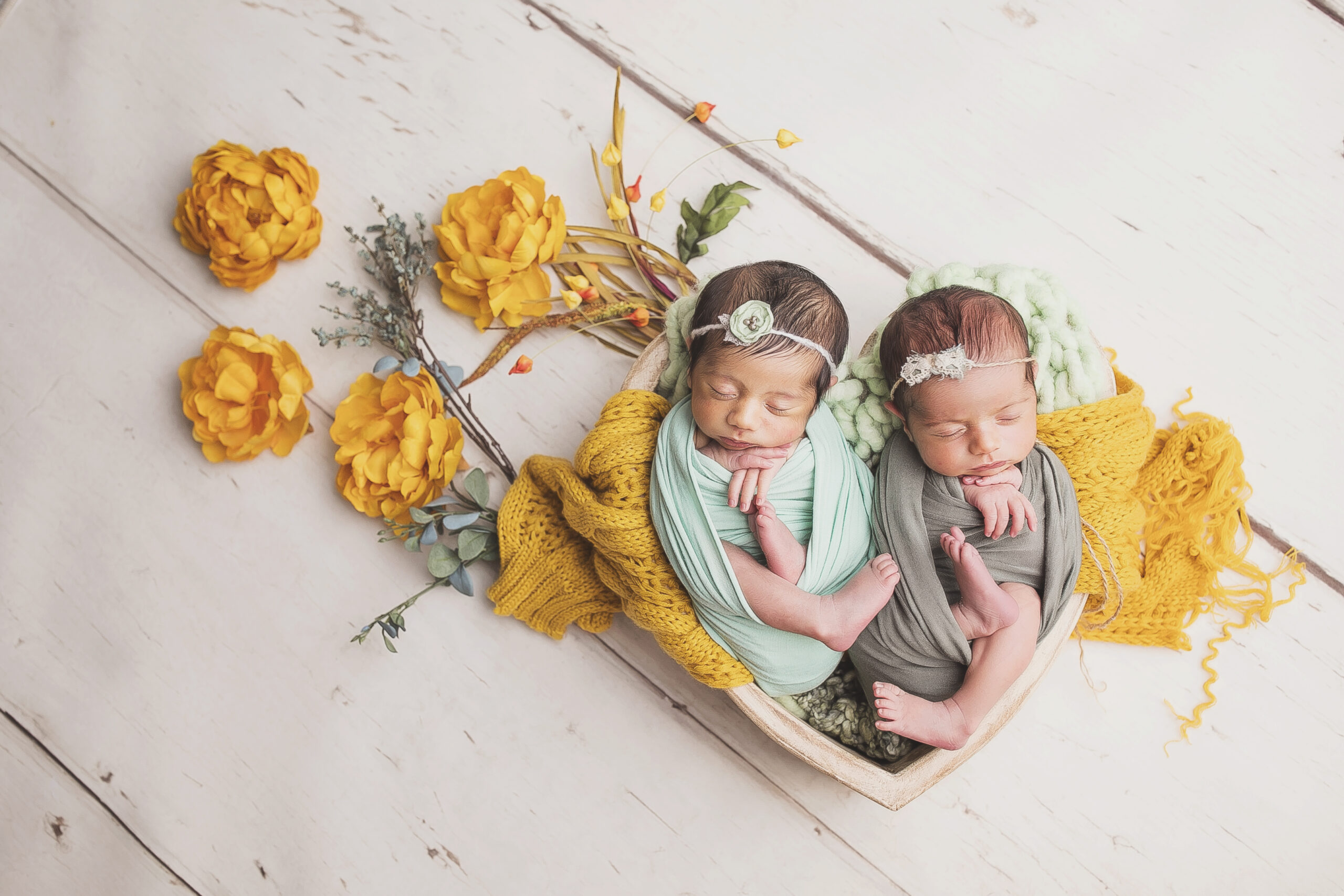Twin babies in wooden heart posing together with yellow flowers by Austin Newborn Photographer, Giselle Salazar