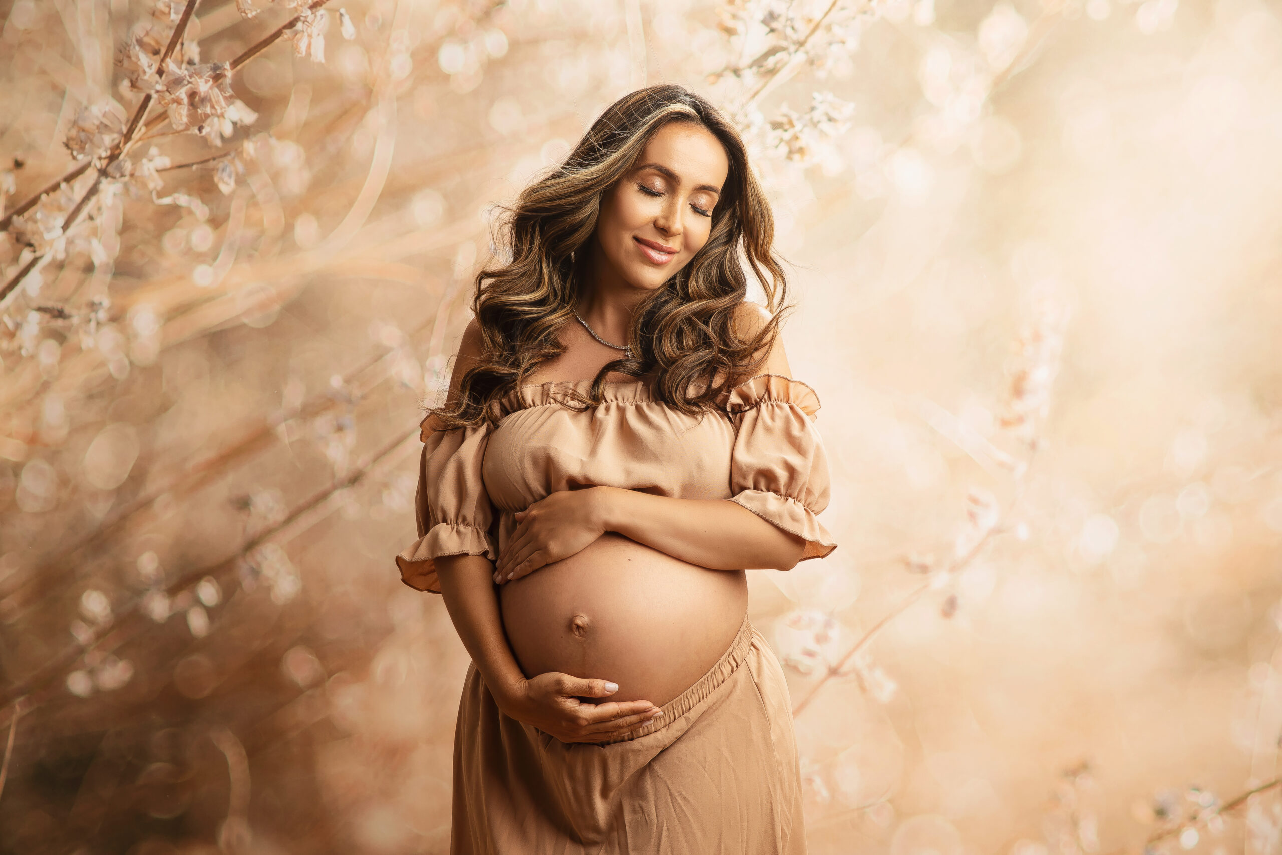 Pregnant Woman holding her belly against floral and beige tones by maternity studio photographer in Austin